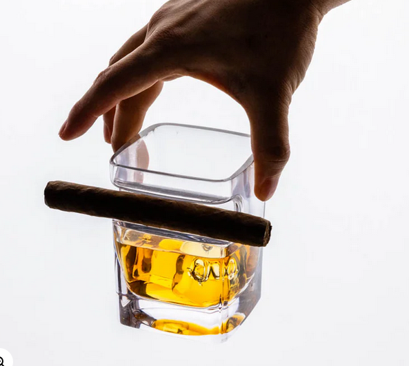 Hand lifting cigar glass with whiskey and cigar