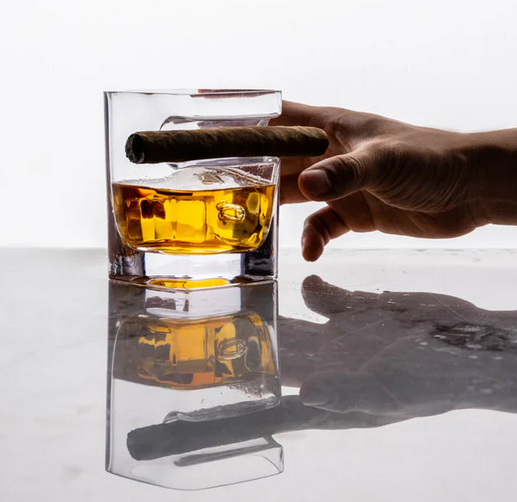 Hand reaching for cigar glass with whiskey